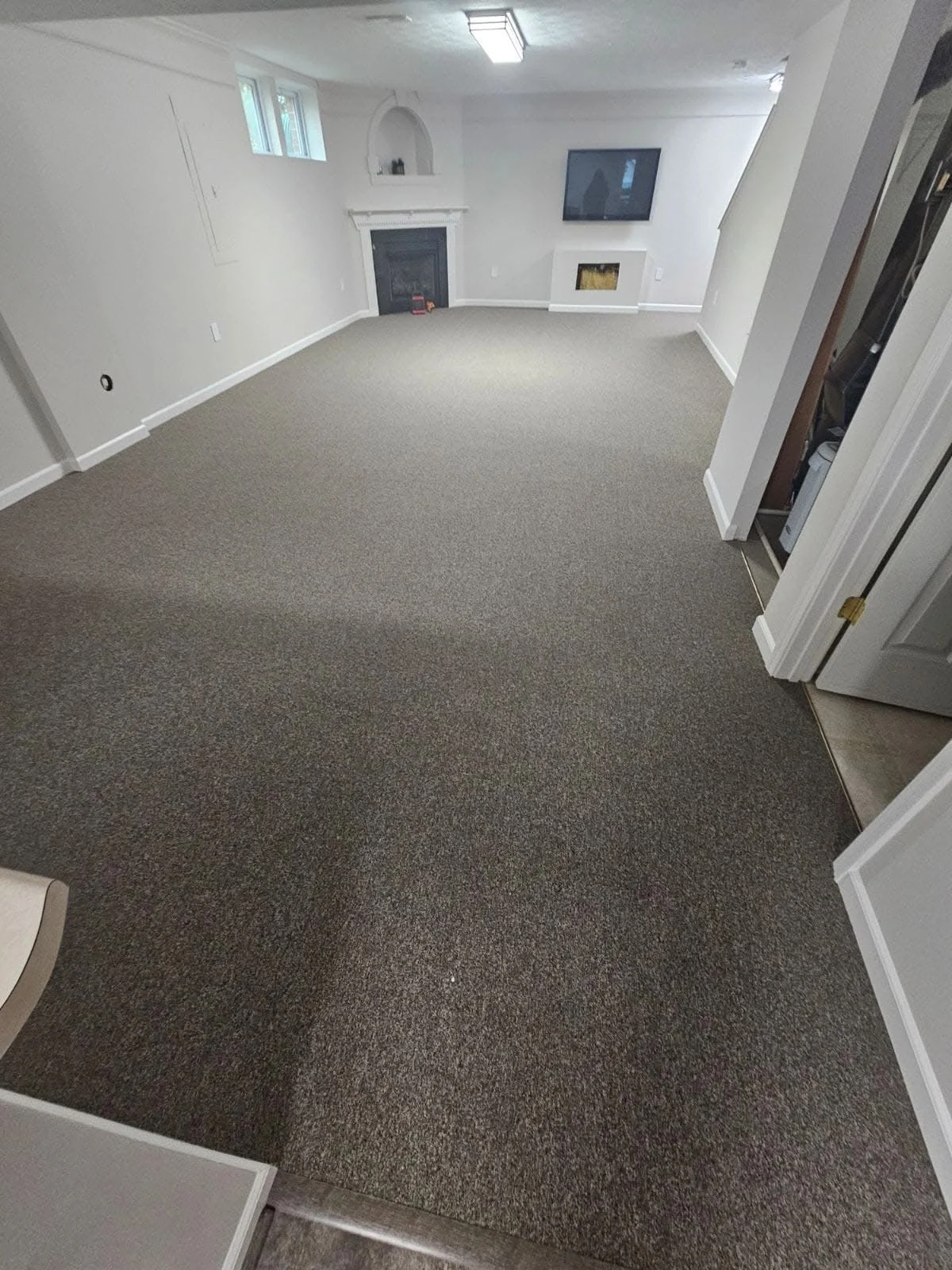 Wall-to-wall carpet installed in a basement room with white walls and a fireplace