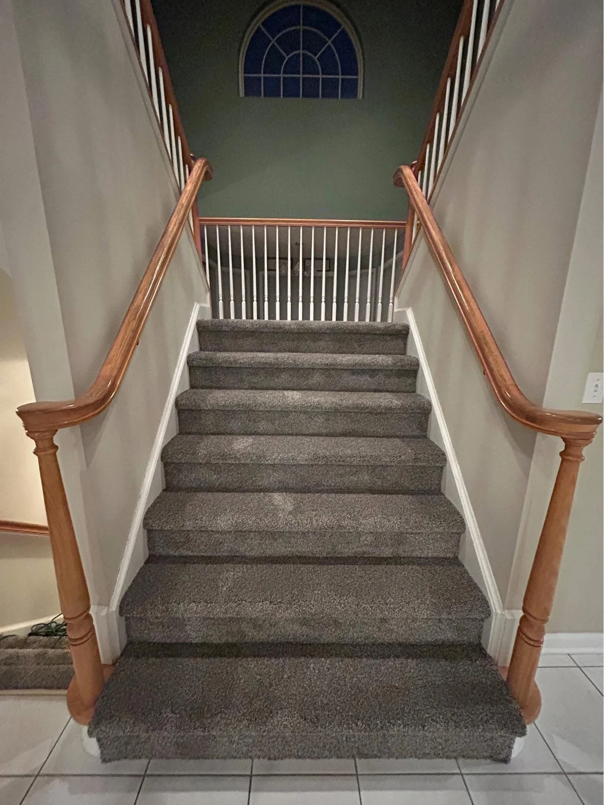 Gray carpet fitted to a staircase with wood handrails and white spindles