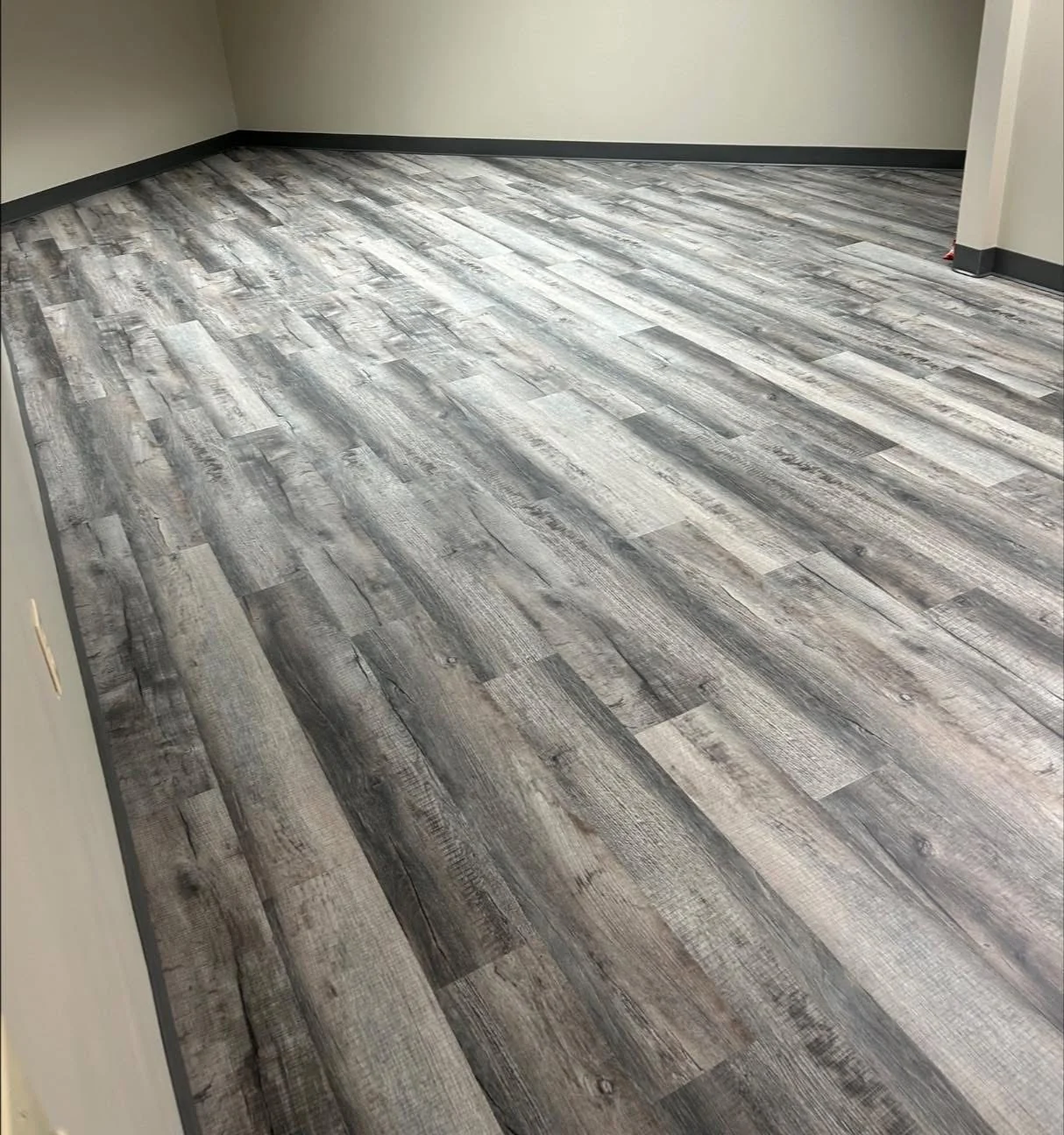Gray wood-look planks installed in a room with dark baseboards