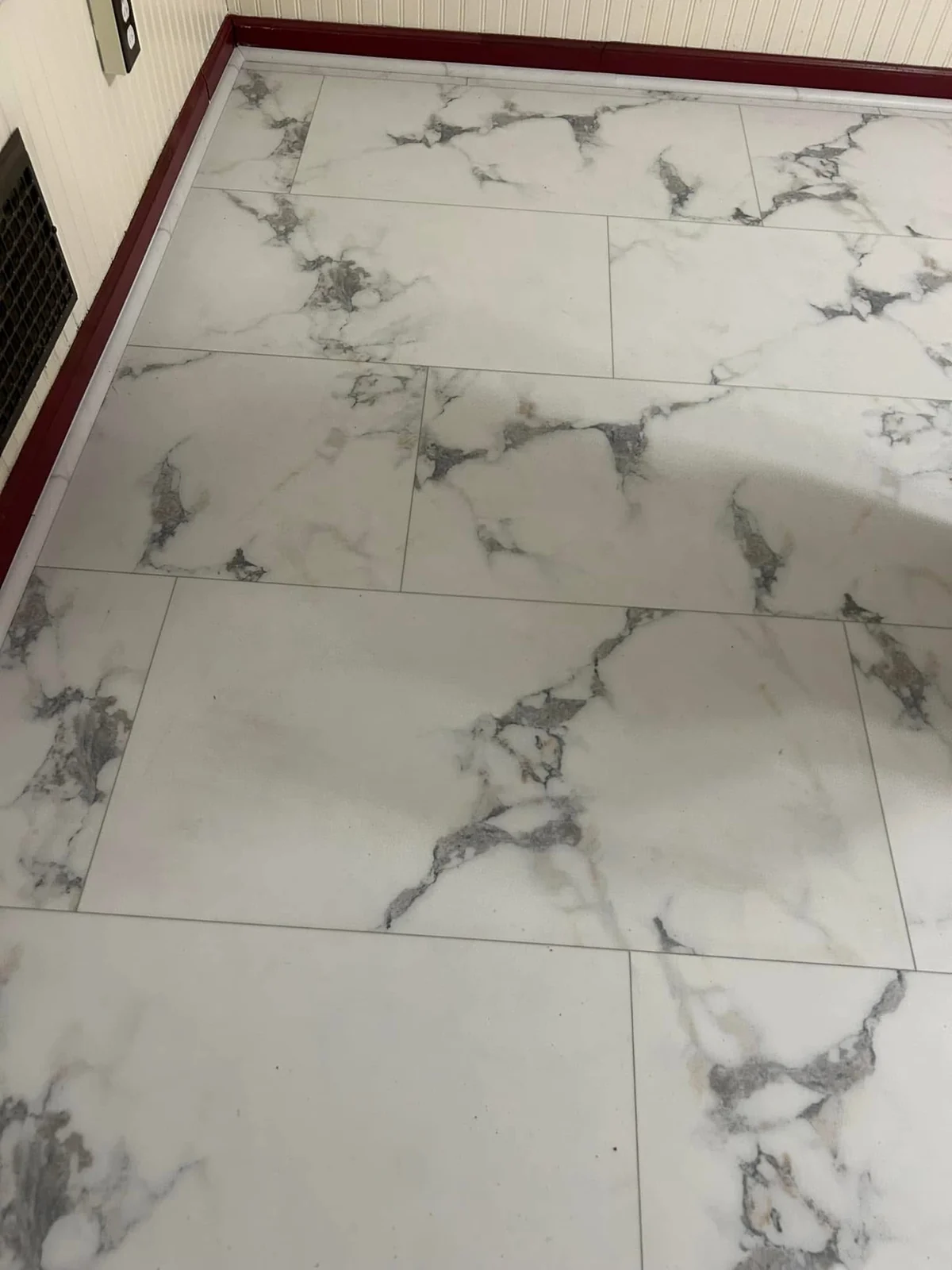 White marble-look flooring with gray veining beside dark wood trim