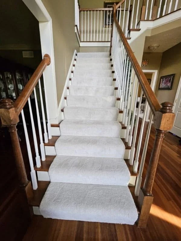 Light carpet runner fitted along a wood staircase with white spindles