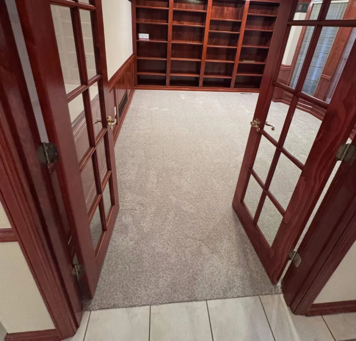 Neutral carpet in a study framed by wood French doors and built-in shelving