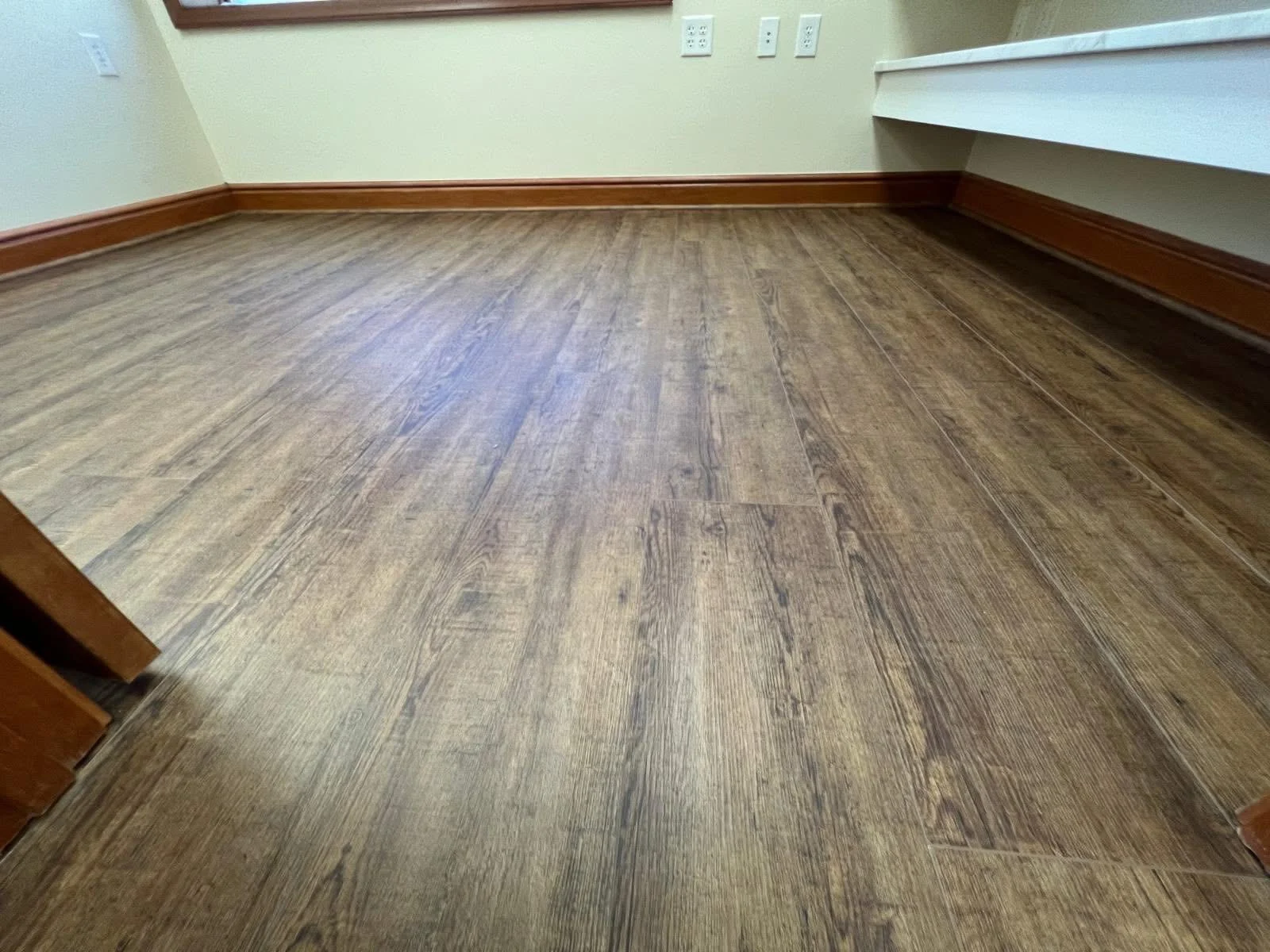 Detailed view of wood-look flooring near wood baseboards and a counter